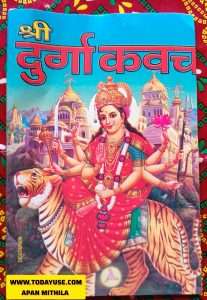 A full-color devotional image on a book cover. The central figure is the Hindu goddess Durga, depicted with multiple arms, riding a tiger. She holds various weapons and symbols, including a sword, trident, and lotus flower. She wears a crown, a red sari, and elaborate jewelry. In the background, several ornate temples or palaces with golden domes are visible against a blue sky. At the top of the image, the title 'श्री दुर्गा कवच' (Shri Durga Kavach) is written in large red Hindi script with a yellow outline, above the illustration. A website URL, 'WWW.TODAYU56.COM', is partially visible at the bottom left, and 'DESIGNER' is written vertically on the left side."Apan Mithila
www.todayuse.com