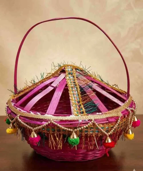 Handmade-woven bamboo basket (known as a Phuldali or Saji). Red colored basket is a staple of Mithila culture in Bihar, India, and is primarily used to carry flowers for religious rituals. The basket features a conical, ventilated lid adorned with gold tinsel, colorful embroidery, and hanging decorative tassels with small metallic bells, topped with a tall, curved handle for easy carrying. todayuse or apan mithila