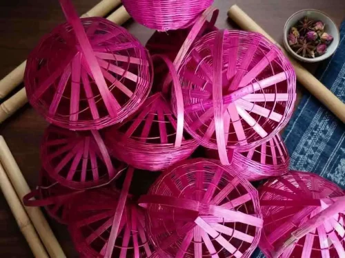 Handmade-woven bamboo basket (known as a Phuldali or Saji). Red colored basket is a staple of Mithila culture in Bihar, India, and is primarily used to carry flowers for religious rituals. The basket features a conical, ventilated lid adorned with gold tinsel, colorful embroidery, and hanging decorative tassels with small metallic bells, topped with a tall, curved handle for easy carrying. todayuse or apan mithilause. www.todayuse.com